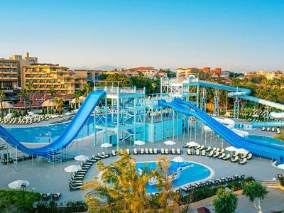 Large water park with slides, pool, and lounge chairs surrounded by palm trees and hotel buildings.