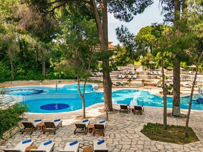 Pool area with sun loungers and trees on paved ground outdoors.