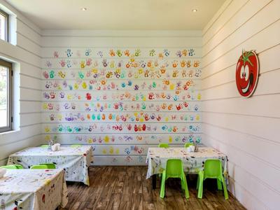 Bright children's playroom with colorful wall decorations and small tables with green chairs.