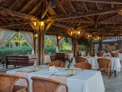 Covered outdoor restaurant area with set tables and wicker chairs at a hotel.