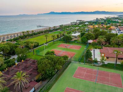 View of tennis courts and coastline with beach and houses at sunset.