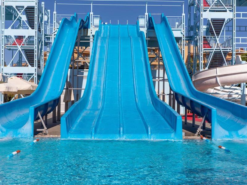 Three blue water slides lead into a pool, surrounded by hotel buildings.
