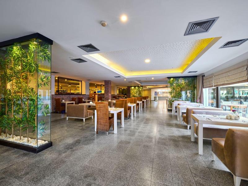 Modern hotel restaurant interior with tables, chairs, and green plants.