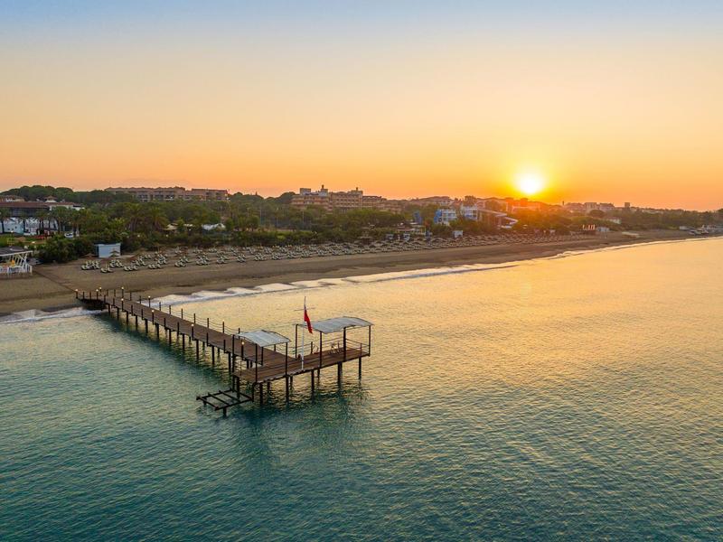 Sunset over a long pier at a calm beach with few houses in the background.