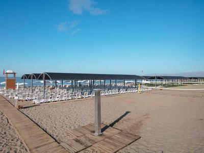 Leerer Sandstrand mit Sonnenschirmen und weißen Liegestühlen unter blassem Himmel.