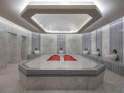 Wnętrze nowoczesnego hammamu z marmurowymi ławkami i eleganckim oświetleniem sufitowym.