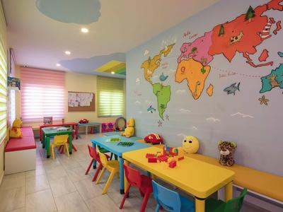 Kolorowy pokój zabaw dla dzieci z stołami, krzesłami i mapą świata na ścianie.