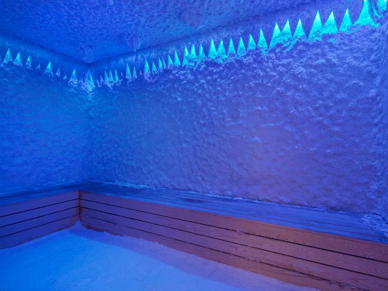 Sauna z teksturowanymi ścianami oświetlonymi na niebiesko i drewnianymi ławkami.