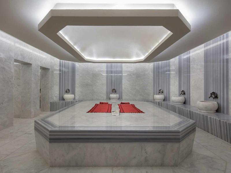 Wnętrze nowoczesnego hammamu z marmurowymi ławkami i eleganckim oświetleniem sufitowym.