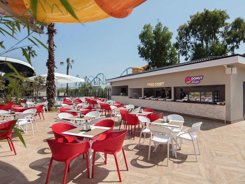 Taras z czerwonymi i białymi stolikami i krzesłami pod parasolami obok otwartego baru.