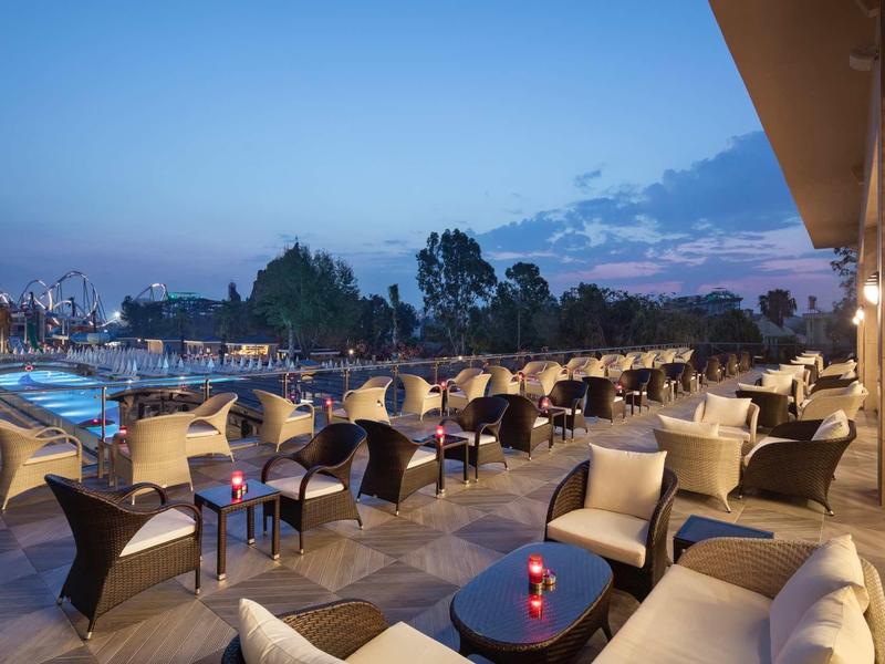 Taras hotelowy z wygodnymi fotelami, stolikami i widokiem na basen o zmierzchu.
