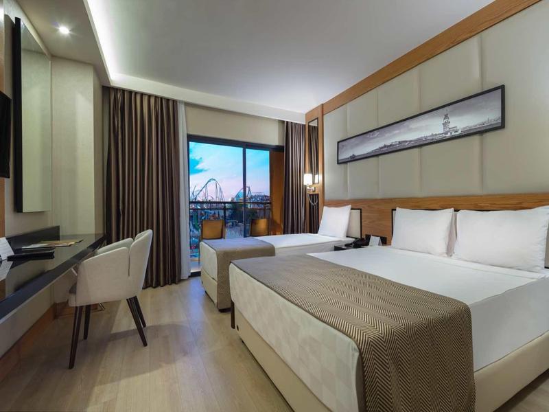 Nowoczesny pokój hotelowy z dużym łóżkiem, biurkiem, telewizorem i balkonem z widokiem na miasto.