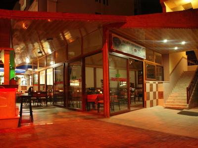 Avondfoto van een restaurant met glazen wanden en rode stoelen naast een trap.