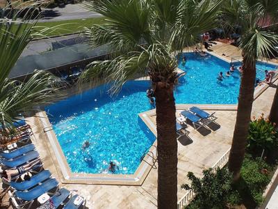 Freizeitbad mit rechteckigem Becken, blauen Liegestühlen und Palmen rundherum.