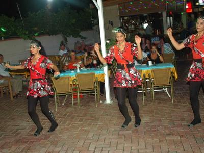Drie vrouwen dansen buiten voor zittende gasten aan gedekte tafels.