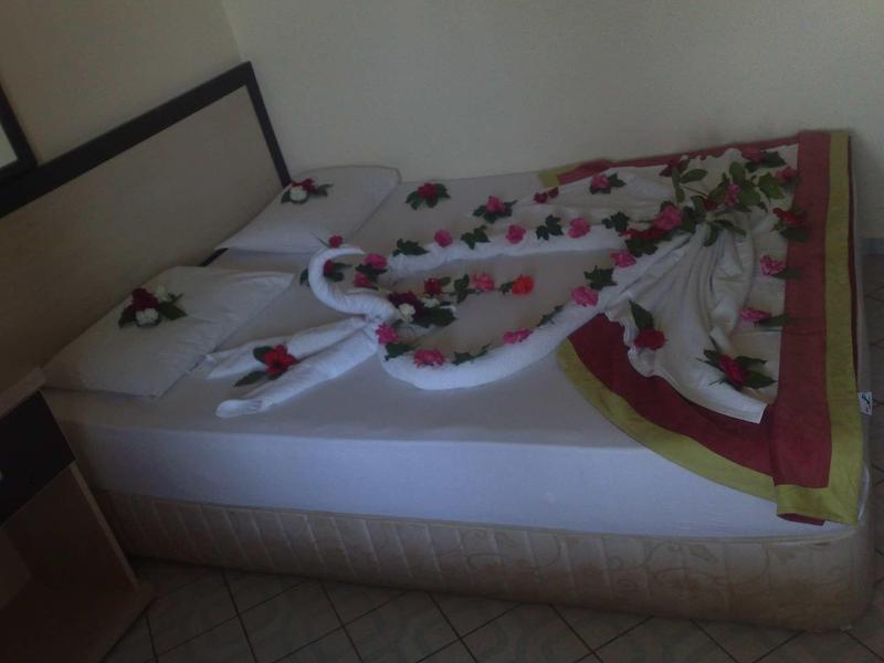 Hotelová postel s dekorativně složeným povlečením ve tvaru srdce a růžovými okvětními lístky