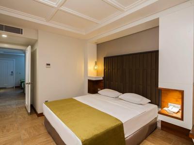 Hell eingerichtetes Schlafzimmer mit Doppelbett, grünem Überwurf, schlichter Dekoration und Holzfußboden.