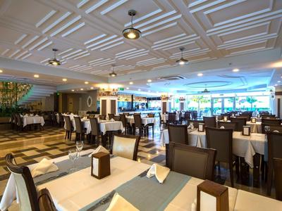 Großer, moderner Speisesaal mit gedeckten Tischen, braunen Stühlen und Tageslicht von Fenstern.