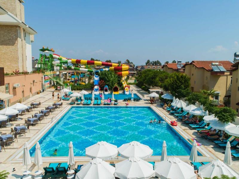 Großer Außenpool mit bunten Wasserrutschen und Sonnenschirmen in sonniger Hotelumgebung.