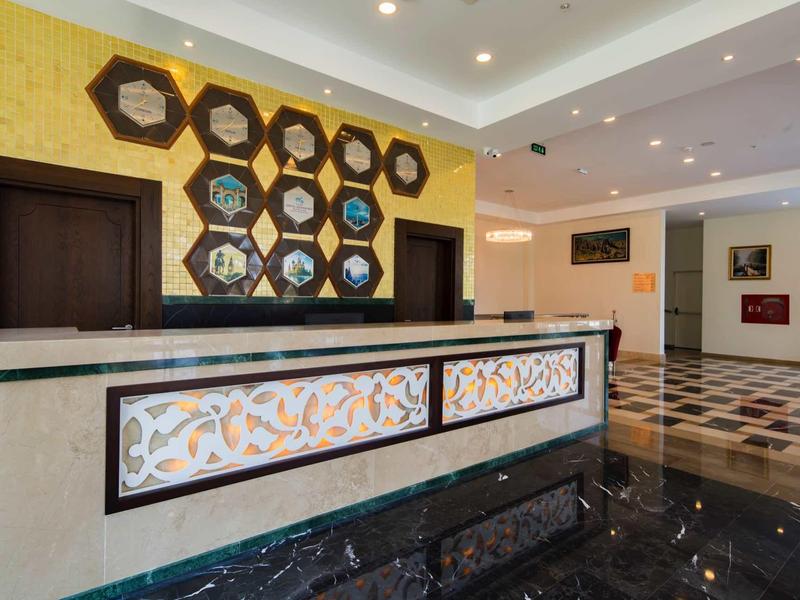 Empfangsbereich mit dekorativem Tresen, sechseckigen Spiegeln an gelber Wand und Marmorfußboden.