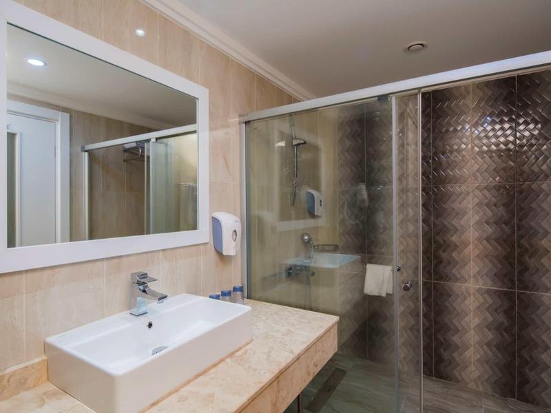 Moderner Badezimmerbereich mit Waschbecken, großer Spiegel, Seifenspender und Dusche mit Glasschiebetür.