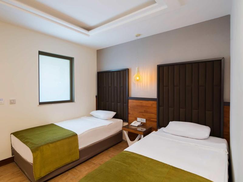 Zweibettzimmer mit weißen Betten, grünen Decken, dunklen Kopfteilen und Holzfußboden.