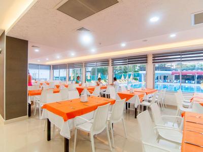 Restaurante iluminado con sillas y mesas blancas, manteles y servilletas naranjas.