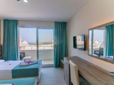 Brightly furnished hotel room with two beds, balcony, and sea view.