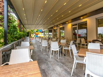 Terraza cubierta de restaurante con sillas blancas y mesas de madera, rodeada de naturaleza verde.