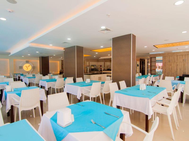 Restaurante moderno y luminoso con sillas blancas y mesas turquesa en un hotel.