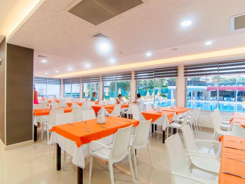 Restaurante iluminado con sillas y mesas blancas, manteles y servilletas naranjas.