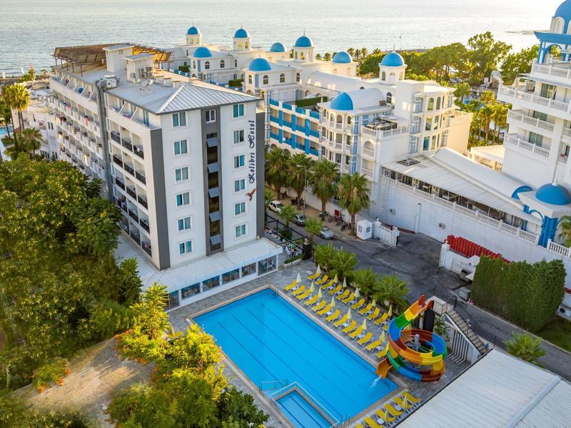 Complejo hotelero moderno con piscina y tobogán en una ubicación costera soleada.