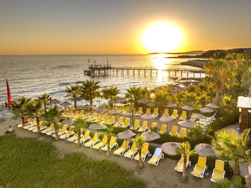 Atardecer sobre el mar con tumbonas y un largo muelle en la playa del hotel.