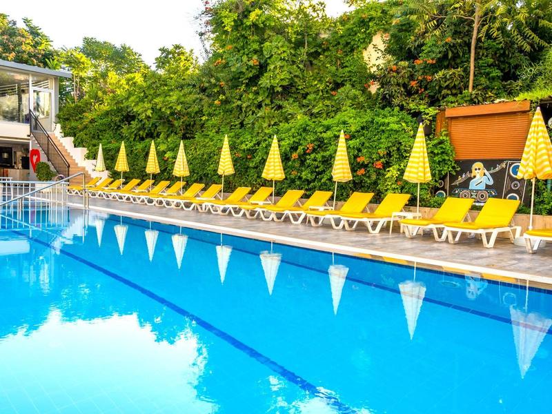 Piscina con agua azul, sombrillas amarillas y tumbonas junto a árboles verdes.