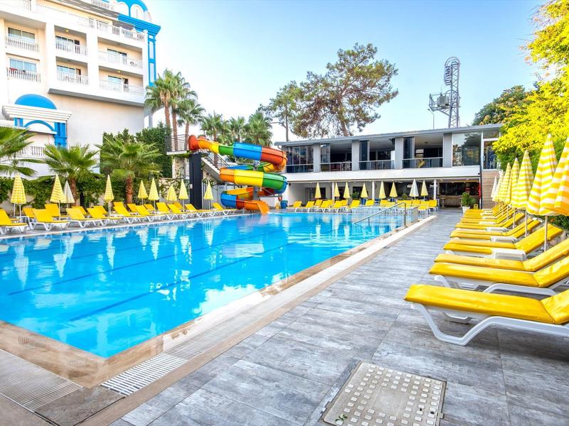 Piscina exterior con tumbonas amarillas y toboganes junto a un edificio hotelero