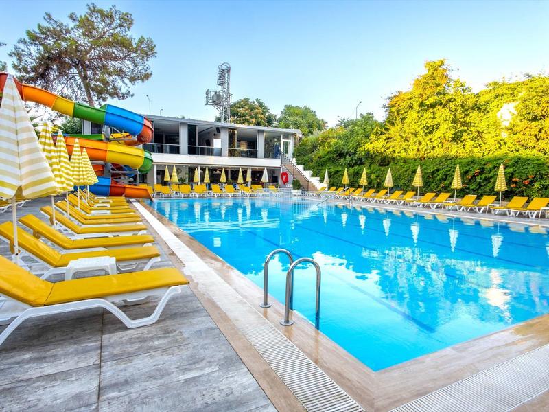 Piscina recreativa al aire libre con toboganes y tumbonas amarillas en un día soleado.