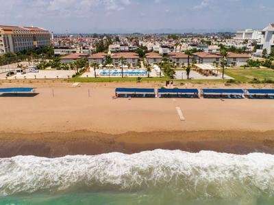 Široká písčitá pláž s lehátky a hotely v pozadí pod modrou oblohou.