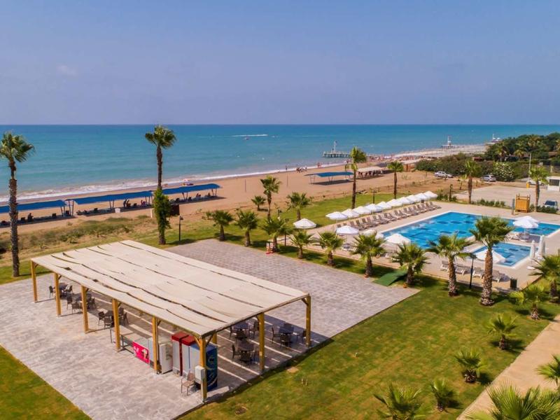 Complejo hotelero con piscina, áreas de descanso cubiertas y vista a una playa de arena y el mar.