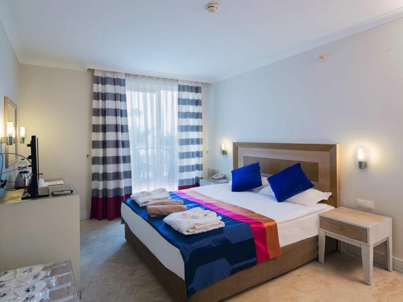 Habitación de hotel moderna con cama doble, corredor de cama colorido y ventana grande con cortinas.