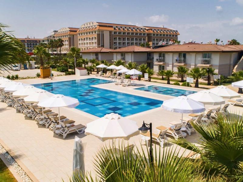 Piscina exterior con tumbonas y sombrillas en un resort hotelero bajo cielo azul.
