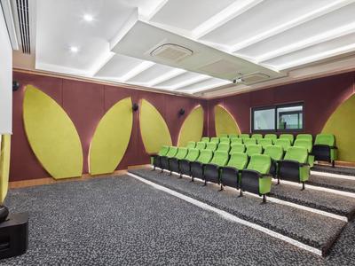 Piccola sala cinema con sedili verdi e pareti decorative gialle e viola.