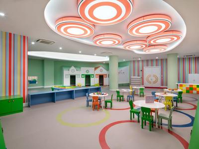 Sala de juegos colorida para niños con mesas pequeñas, sillas y luces de techo cerca del hotel.