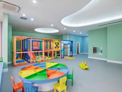 Sala de juegos infantil colorida con estructura para escalar, mesa redonda para pintar y sillas pequeñas en habitación luminosa.