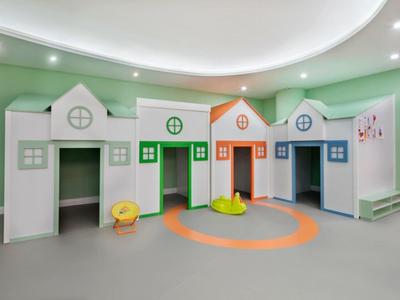 Área de juegos para niños con estructuras de juego en forma de casas de colores en una habitación verde.
