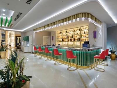 Área moderna de bar de hotel con barra verde, sillas rojas e iluminación elegante.