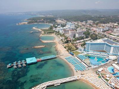 Vista aérea de un hotel costero con piscinas, playa y muelles para botes en agua clara.