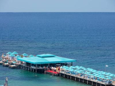 Un largo muelle con sombrillas turquesas se extiende sobre el mar azul en un día despejado.