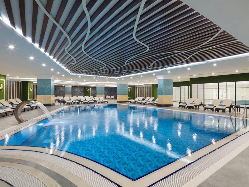 Gran piscina cubierta iluminada con tumbonas y techo moderno en un hotel.