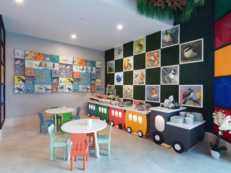 Habitación infantil con sillas y mesas coloridas y un tren de juguete en la pared.