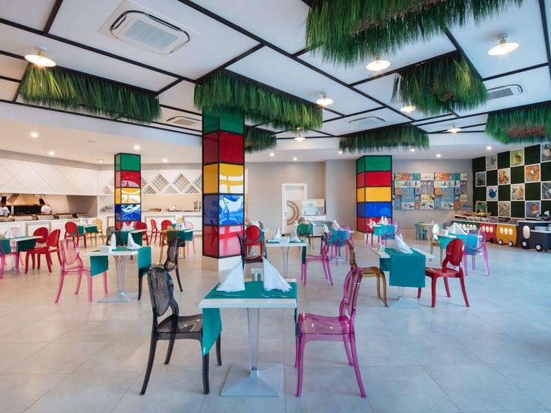Amplio comedor luminoso con sillas de colores y decoraciones verdes en el techo.